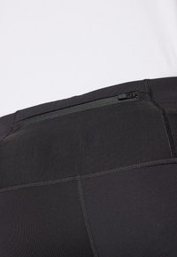 Svarta atletiska leggings med en texturerad midja, en liten dragkedjeficka bak och ett mjukt, elastiskt tyg.