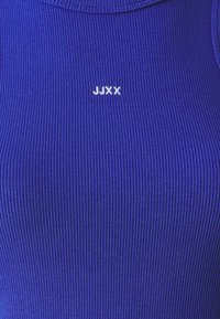 Close-up of ribbed dark blue fabric with small white embroidered text "JJXX" centered near the top.