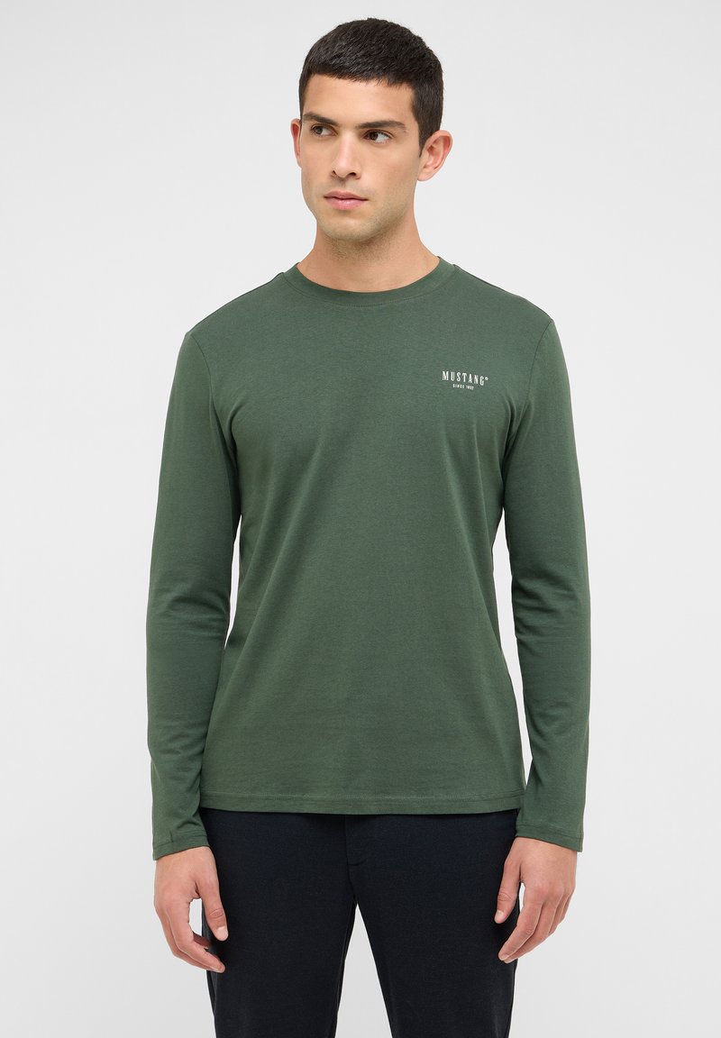 Grøn langærmet t-shirt lavet af blød bomuld, med en lille hvid "MUSTANG"-logo trykt på venstre brystområde. Glat tekstur.