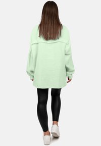 Camicetta oversize verde menta con tessuto testurizzato, spalle scese e maniche lunghe, abbinata a leggins neri e sneakers bianche.