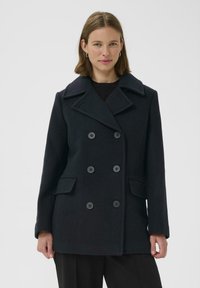 Juodasis vilnonis paltas su dvigubu užsegimu, didelėmis sagomis, plačia apykakle ir dviem priekiniais kišenėmis. Lygus audinys ir pritaikytas siluetas.