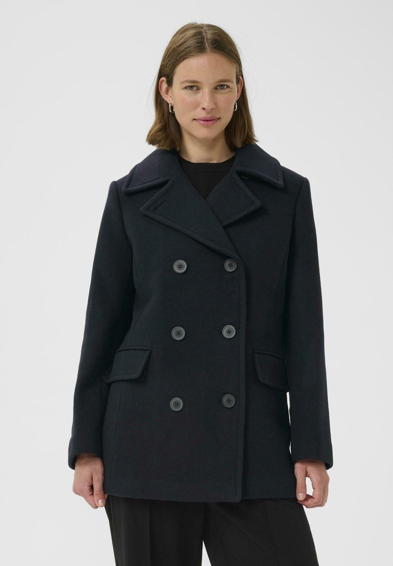 Juodasis vilnonis paltas su dvigubu užsegimu, didelėmis sagomis, plačia apykakle ir dviem priekiniais kišenėmis. Lygus audinys ir pritaikytas siluetas.