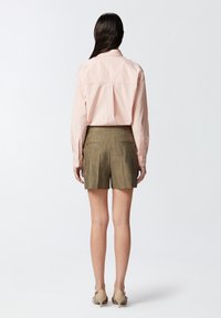 Svijetlo ružičasta prugasta košulja s krojenim leđima, uparena s maslinasto zelenim, teksturiranim šortsevima s džepovima; nosi se s bež štiklama.