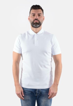 Polo shirt bianco a maniche corte con colletto, dotato di una patta con tre bottoni e un discreto dettaglio del logo, abbinato a jeans blu.