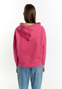 Felpa cropped rosa con cappuccio regolabile e polsini a costine. Abbinata a jeans di denim blu chiaro. Tessuto morbido, design semplice.