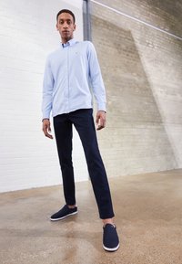 Ljusblå button-up skjorta, marinblå byxor och mörka slip-on skor. Slätt tyg, skräddarsydd passform och subtila märken på skjortan.