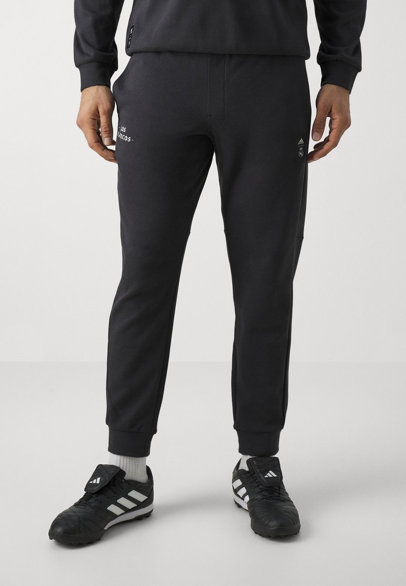 Pantalones de chándal negros de corte ajustado, hechos de un tejido suave. Presentan detalles de logo y puños en los bordes. Combinados con zapatillas deportivas en negro y blanco.