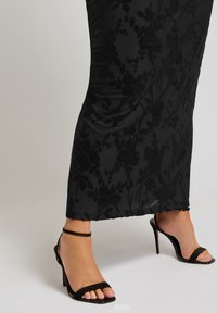 Svart blommig spetsklänning med satinfinish som sträcker sig ner till anklarna. Kombinerad med svarta remsandaler med smala stilettklackar.