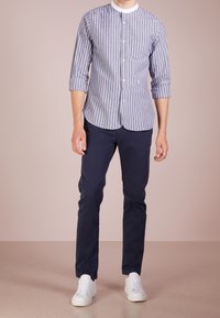 Camicia a righe con colletto bianco, pantaloni aderenti blu marino e sneakers bianche. La camicia presenta righe verticali blu e bianche.