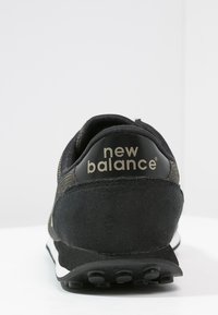 Czarne buty biegowe z zamszową i siatkową cholewką, zaokrąglonym obcasem oraz białą podeszwą środkową z teksturowaną gumową podeszwą zewnętrzną. Logo "New Balance" na obcasie.