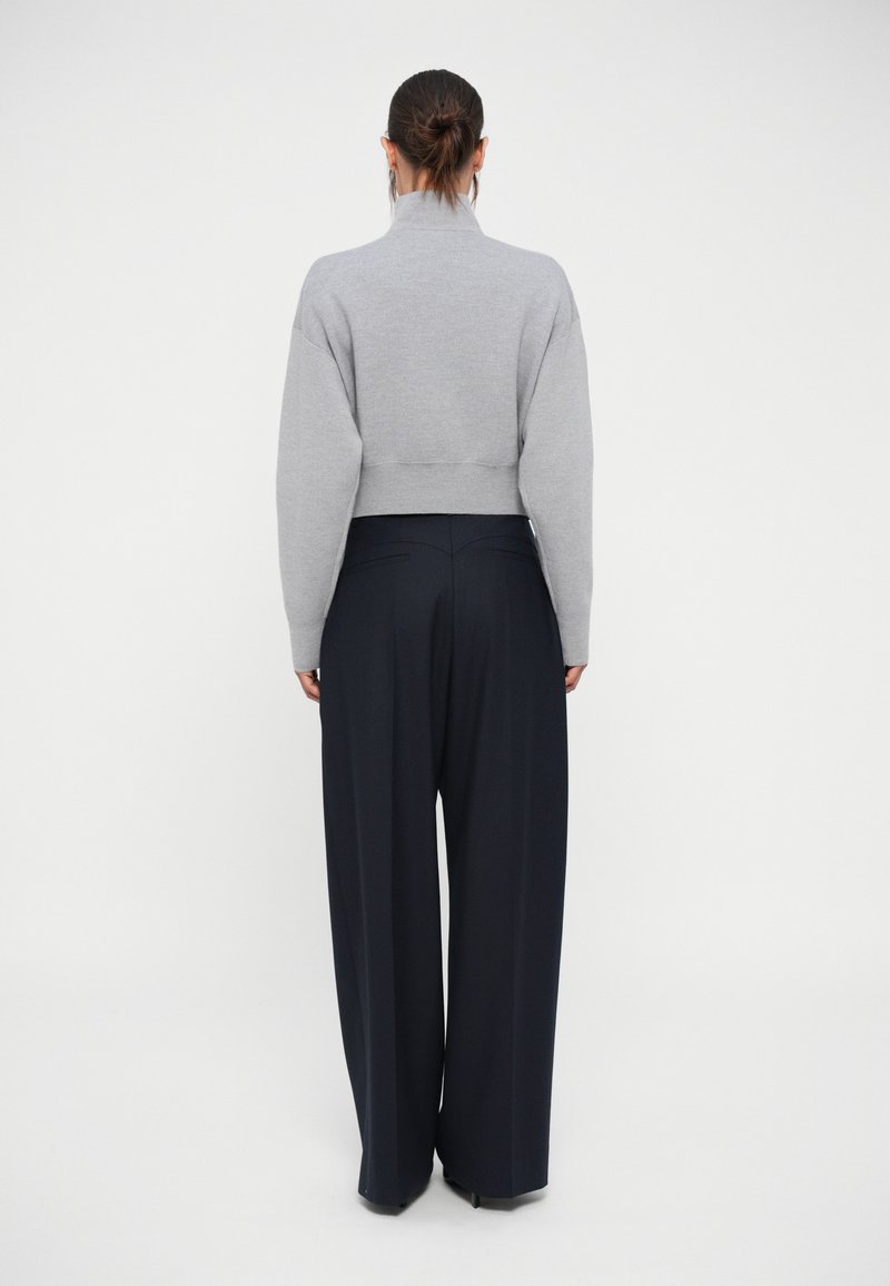 Pull cropped gris avec un col haut et des manches larges associé à un pantalon large bleu marine. Texture en maille lisse, détails minimaux.