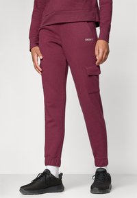 Pantaloni de sport maron cu manșete ribbed, talie elastică și buzunare laterale. Logo-ul notabil DKNY pe coapsă. Textură moale a materialului.