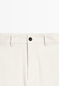 Pantaloni beige con fronte piatto, chiusura con bottone e passanti per cintura. Realizzati in tessuto morbido con sottili dettagli di cucitura.