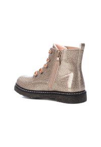 Botín brillante en color beige con cordones en la parte delantera, ojales decorativos y cremallera lateral. Presenta una suela de goma negra y un forro color marrón claro.