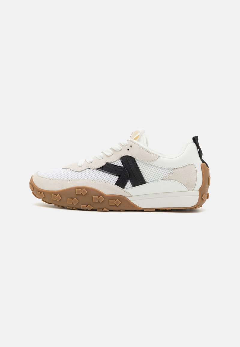 Hvite og beige mesh sneakers med svarte detaljer, teksturert semsket skinn og en brun gummisåle med et grep mønster.