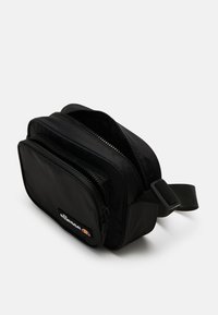 Černá nylonová taška přes rameno s dvěma zipovými přihrádkami, odolným švem a nastavitelným popruhem. Logo značky zobrazeno na přední straně.