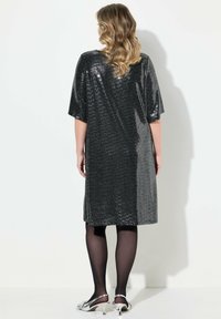 Schwarzes Pailletten-Kleid mit lockerer Passform und kurzen Ärmeln. Glatte Textur, knielanger Saum, modisch kombiniert mit schwarzen Strumpfhosen und silbernen Schuhen.
