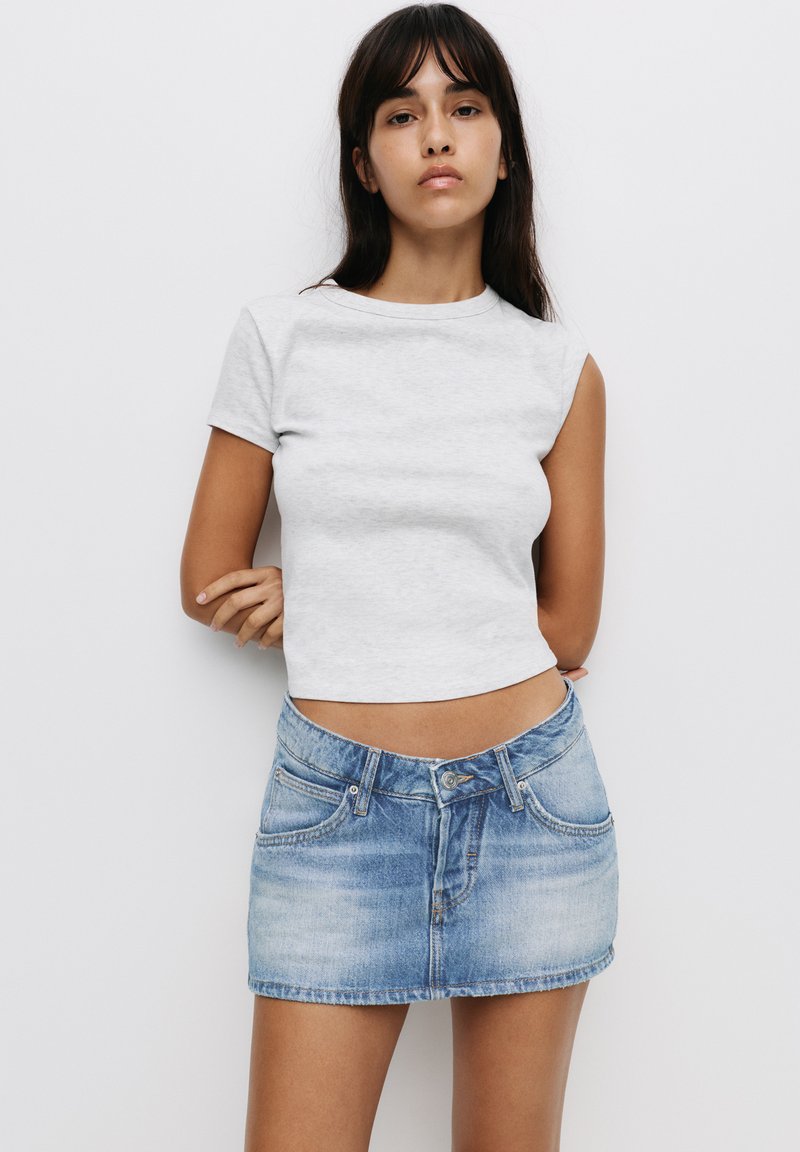 T-shirt grise coupée avec des manches courtes associé à une mini-jupe en denim bleu clair. Le tissu semble doux et le design est simple et ajusté.
