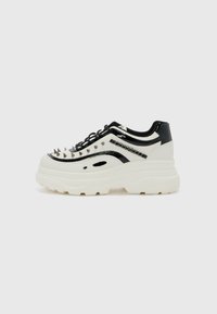 Zapatillas chunky con materiales sintéticos en blanco y negro, que presentan puntas plateadas en la punta y una suela gruesa blanca con un dibujo texturizado.