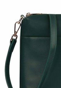 Ramenní taška z tyrkysové kůže s hladkou texturou, vybavená jemným švem a zlatým kováním na uchycení popruhu.