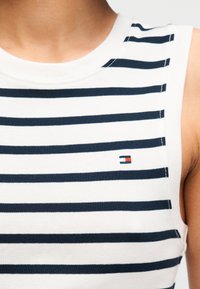 Λευκό και ναυτικό μπλε ριγέ αμάνικο τοπ, κατασκευασμένο από βαμβάκι, με ριμπ λαιμόκοψη και μικρό κεντημένο λογότυπο σε κόκκινο και μπλε.