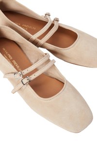 Ballerines en daim beige avec deux boucles de strap, bout rond et texture douce, dotées d'une semelle en cuir et d'un design minimaliste.