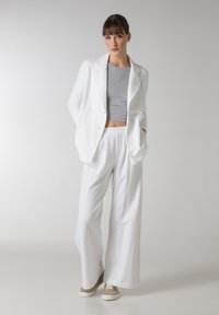 Blazer alb cu două rânduri de nasturi, într-o croială lejeră, asociat cu un top gri scurt și pantaloni albi largi. Pantofii bej completează ținuta.