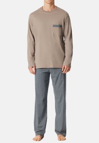 Beige lange mouwen top met een zak en blauwe geometrische patronen, gecombineerd met blauwe gemusterde pyjamabroek. Zachte stof en relaxte pasvorm.