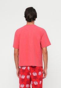 Camiseta de algodón roja con mangas cortas y corte recto, combinada con pantalones rojos de diseño floral. Diseño sencillo y textura suave.