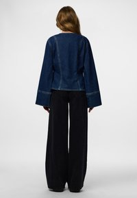 Denimist jakk, millel on vormitud korsett, lehvivate varrukatega ja kontrastõmblused. Tagakülg näitab ümarat kaelusjoont ja sujuvat kangapinda.