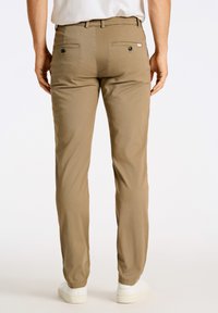 Chinos caqui con perneras rectas, dos bolsillos traseros y una textura sutil. Terminados con un lazo para el cinturón y combinados con zapatillas blancas.