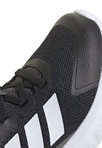 Chaussure de sport noire avec dessus en maille texturée, accents en caoutchouc et bandes de marque blanches. Dispose d'une épaisse semelle blanche et de lacets robustes.