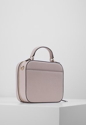 Petit sac à main carré en cuir rose clair avec poignée supérieure et fermeture éclair dorée, posé sur un piédestal blanc sur fond uni.