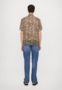 Camisa de manga corta con un patrón de estampado de leopardo y una banda negra "JUST CAVALLI" en la parte inferior, combinada con unos jeans de mezclilla azul claro.