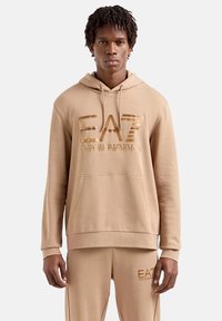 Hoodie beige con tasca anteriore, cappuccio con coulisse e stampa del logo metallica. Realizzato in tessuto morbido con vestibilità rilassata.