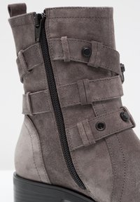 Gray suede ankle boot featuring a side zipper, decorative straps with buttons, and a textured surface. Block heel for stability.