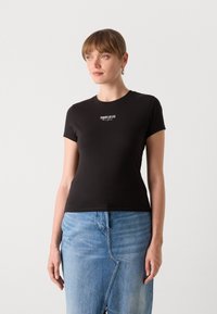 Černé tričko s krátkým rukávem vyrobené z bavlny, s bílým logem "TOMMY JEANS New York" na hrudi. Úzký střih, kulatý výstřih.