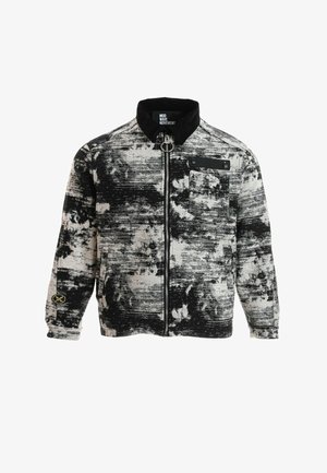 Chaqueta abstracta de patrón en blanco y negro con cremallera, cuello negro, bolsillo en el pecho y pequeño parche con logo en el puño de la manga izquierda.