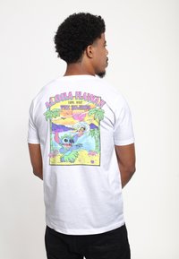 White short-sleeve t-shirt featuring a colorful graphic on the back, depicting a cartoon character and tropical scene with palm trees.
