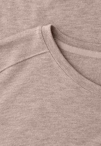 Primer plano del cuello redondo y la costura del hombro de un suéter beige de punto, mostrando una textura acanalada fina y detalles de tela suave.