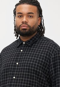 Camisa xadrez preta e branca feita de tecido, com gola abotoada e botões brancos, com um corte descontraído e textura macia.