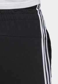 Svarta idrottsshorts med elastisk midja, prydda med tre vertikala vita ränder på sidorna för en sportig design.