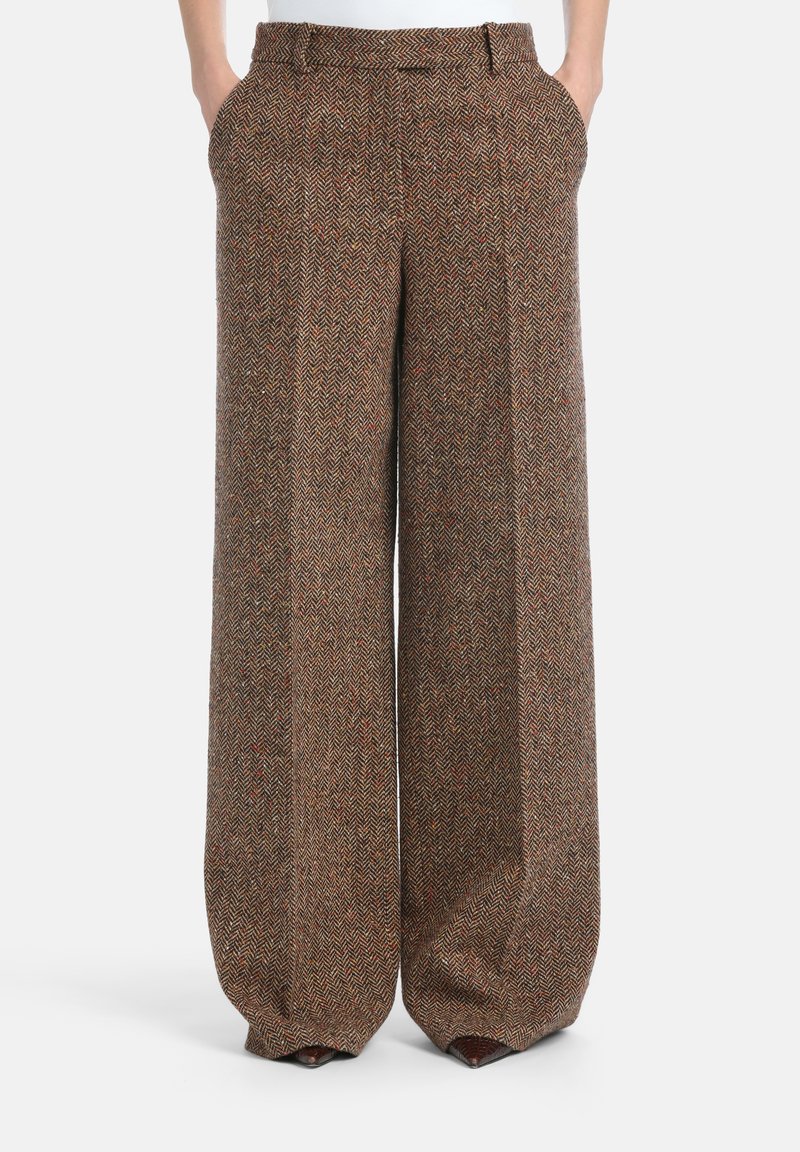 Plaša piegriezuma bikses no brūna vilnas auduma ar hūnstūdu rakstu un smalkiem oranžiem akcentiem. Tām ir divas sānu kabatas un plakans jostas atbalsts.