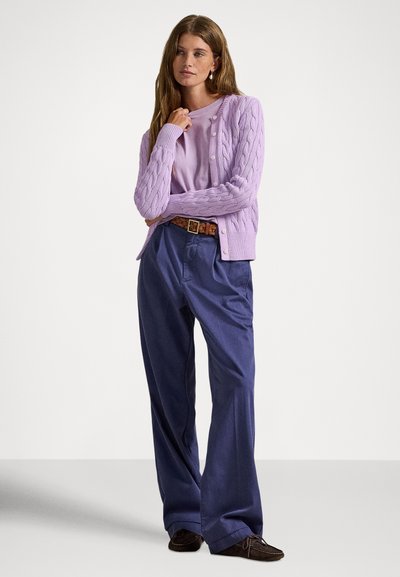 Ανοιχτό μωβ πλεκτή ζακέτα με σχέδιο κοτσίδα πάνω από ένα λιλά τοπ, συνδυασμένη με ναυτικά φαρδιά παντελόνια και καφέ suede παπούτσια. Καφέ υφαντή ζώνη ως στοιχείο έμφασης.