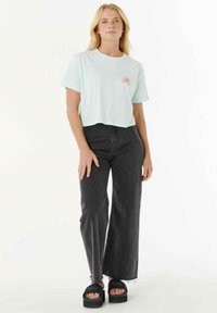 Muntgroene cropped t-shirt met zonafbeelding, gecombineerd met hoog getailleerde zwarte wijde jeans en zwarte platform sandalen.