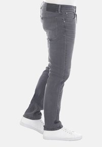 Grijze denim jeans met een slim fit, vijf zakken ontwerp en subtiele wassing. Heeft een zwarte tailleband en contrasterende stiksels. Witte sneakers.