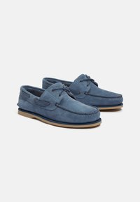 Niebieskie zamszowe mokasyny z haftowanym wzorem, sznurówką i beżową gumową podeszwą. Okrągły nosek i miękka tekstura. Odpowiednie do codziennych stylizacji.