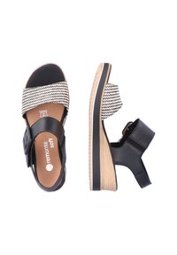 Sandales à bout ouvert noires et crème avec une empeigne à motifs, une bride ajustable, un talon en bois et une semelle en caoutchouc. Comprend une semelle intérieure confortable.