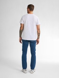 Tricou cu mâneci scurte, în dungi, de culoare albă cu linii pastelate, combinat cu blugi slim-fit albaștri și adidași albi. Tatuaje vizibile pe brațe.