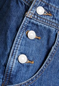 Tissu en denim bleu avec trois boutons métalliques argentés Levi Strauss et coutures oranges sur une poche de veste ou de jeans.